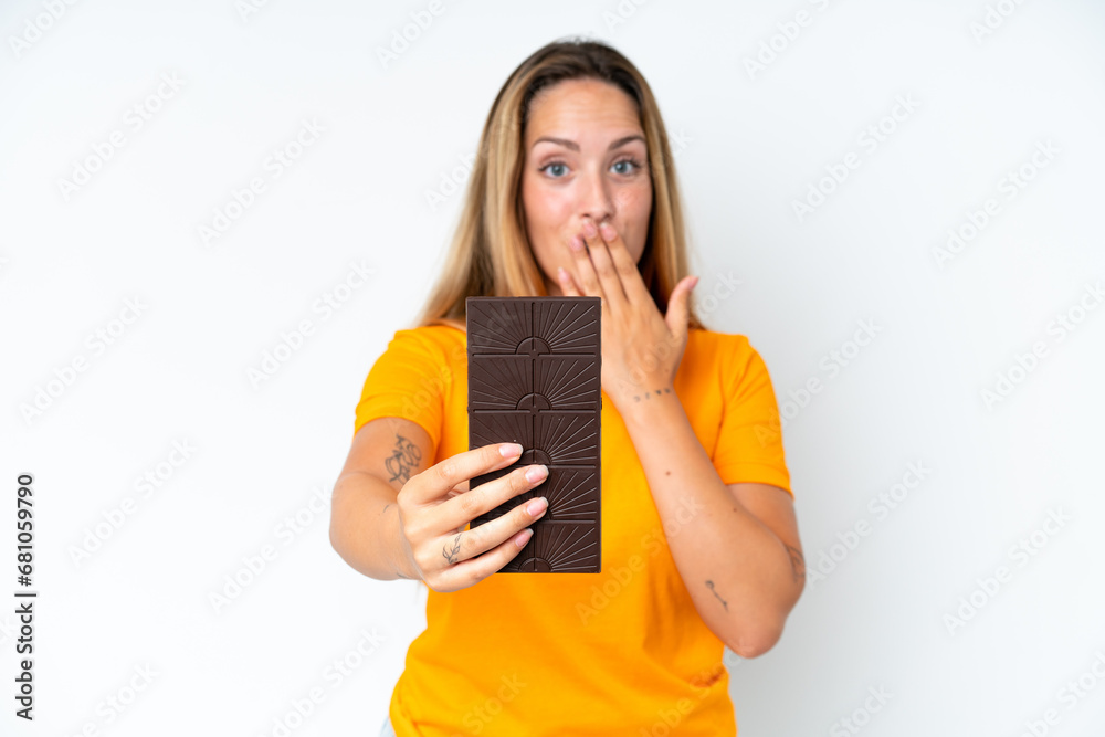 Young caucasian woman isolated on white background taking a chocolate tablet and surprised Young caucasian woman isolated on white background taking a chocolate tablet and surprised