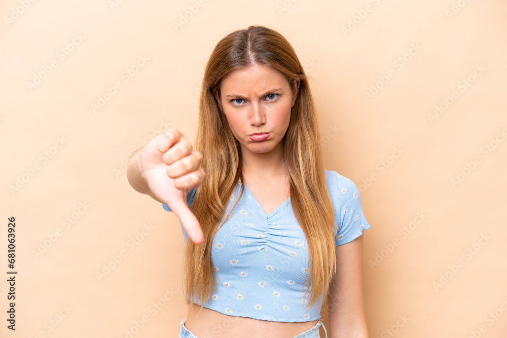 Young caucasian woman isolated on beige background showing thumb down with negative expression
