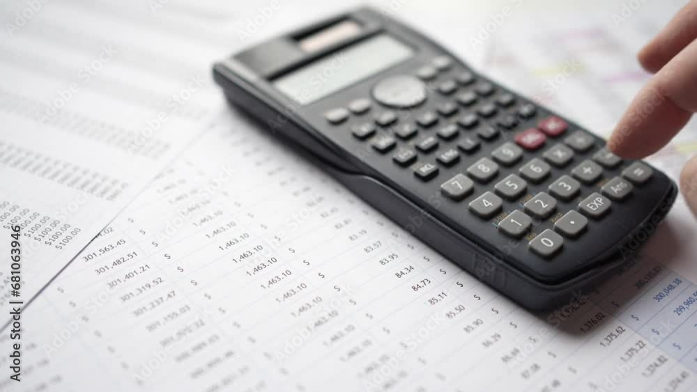 Hand Using a Calculator Over Finance Spreadsheet Documents Hand Using a Calculator Over Finance Spreadsheet Documents