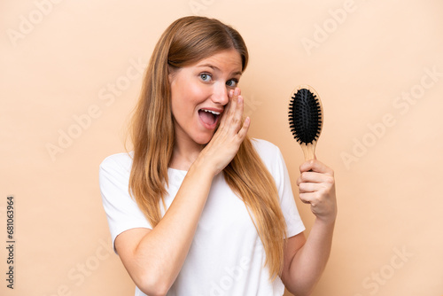 Young pretty blonde woman with hair comb isolated on beige background whispering something