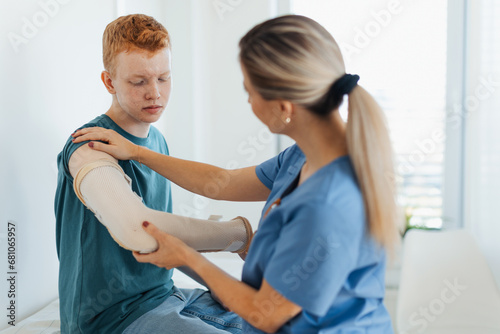 Doctor checking the orthopedic cast, brace on a teenage patient's broken arm. Teenage boy is healing a fracture after an accident.