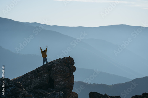 Happy woman in yellow jacket standing on rock with arms spread out. Space for text. © Maria