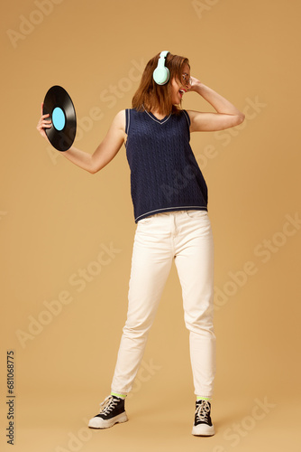 Happy young smiling woman in headphones holding retro vinyl player against beige studio background. Concept of young, human emotions, lifestyle, fashion, music, hobby © master1305