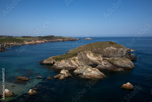 a rocky coastline with a small island covered in greenery  clear blue water  and a clear blue sky