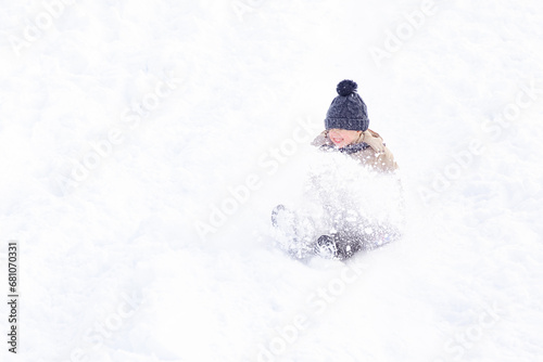 Happy boy slides down an ice slide in winter outside. A little boy rides downhill on a sled in winter. Christmas holidays child outdoor activities.
