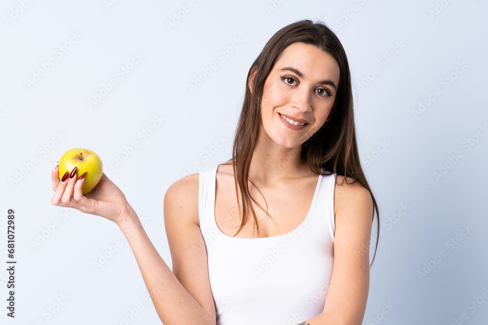 Young woman over isolated blue background with an apple and happy Young woman over isolated blue background with an apple and happy