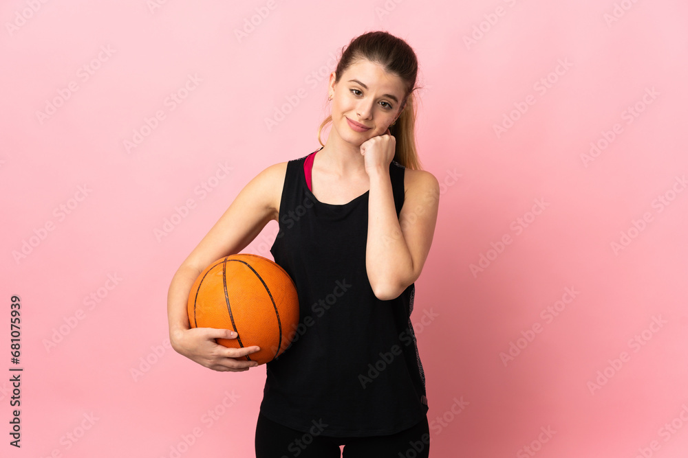 Young blonde woman playing basketball isolated on pink background and looking up