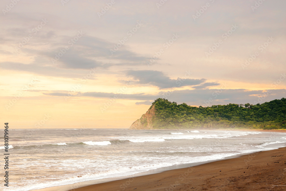 Waves breaking on the beach, with a rocky point in the background, in Costa Rica.