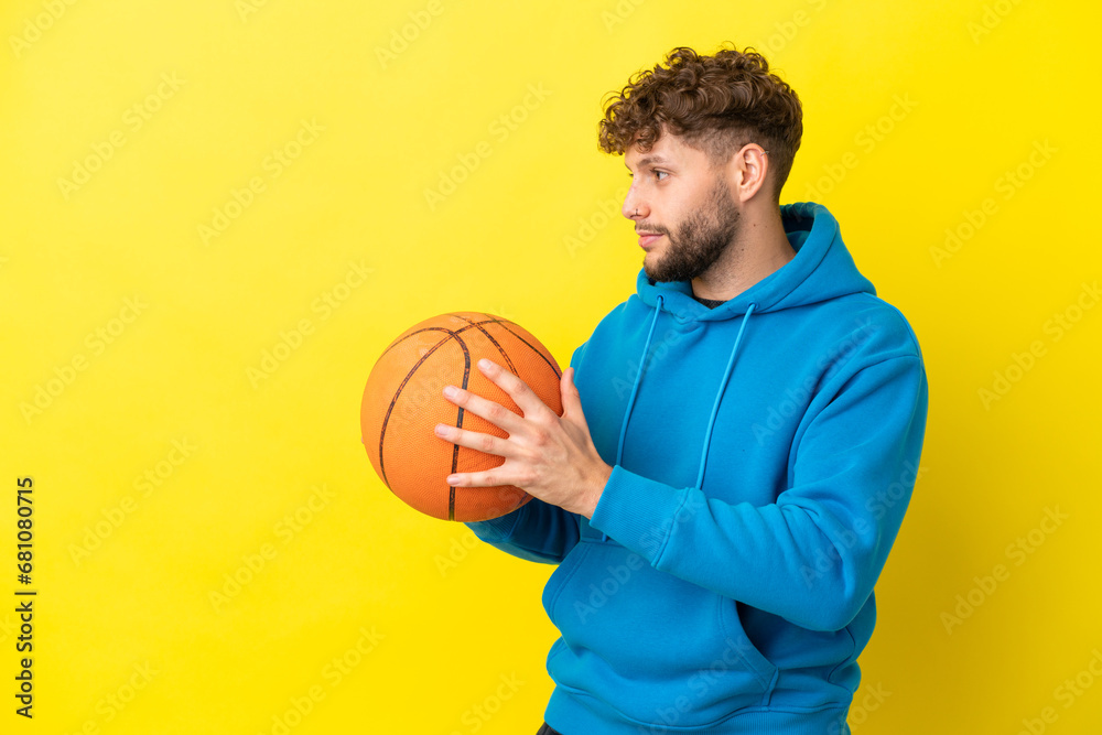 Young handsome caucasian man isolated on yellow background playing basketball Young handsome caucasian man isolated on yellow background playing basketball