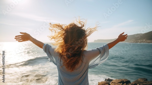 Rear view close up of a woman with arms outstretched facing the ocean.