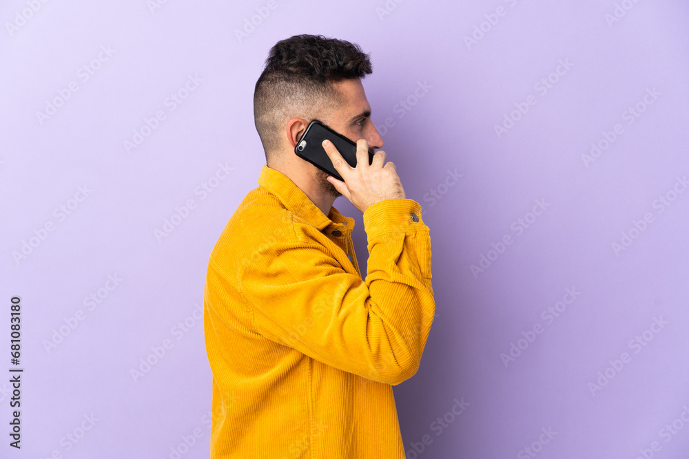 Caucasian man isolated on purple background keeping a conversation with the mobile phone with someone Caucasian man isolated on purple background keeping a conversation with the mobile phone with someone