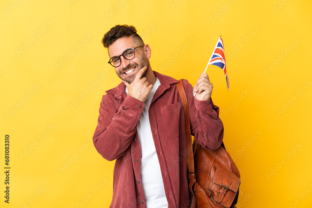 Caucasian man holding an United Kingdom flag isolated on yellow background happy and smiling