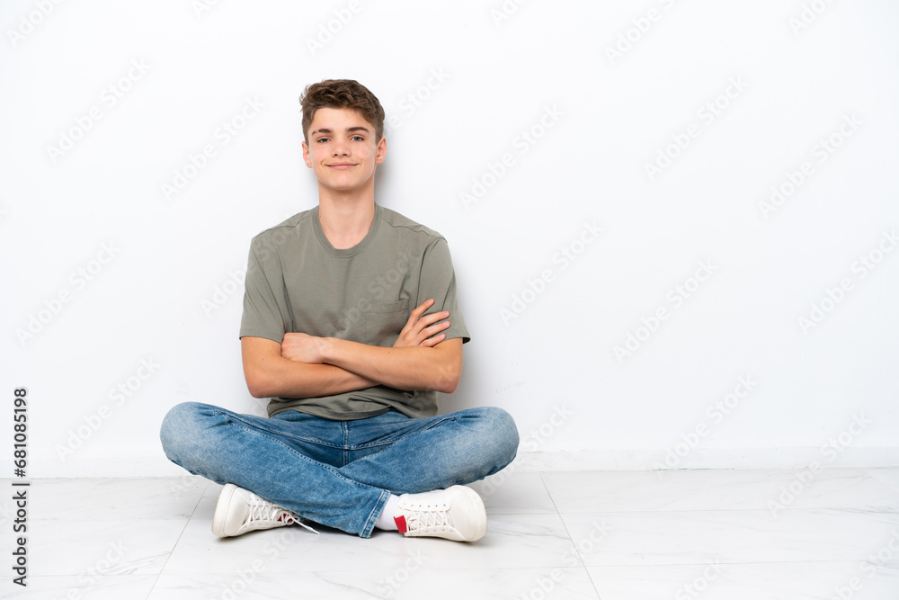 Teenager Russian man sitting on the floor isolated on white background with arms crossed and looking forward