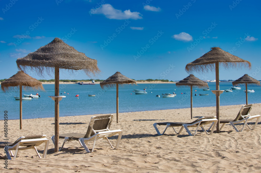 Straw umbrellas and sun loungers on the beach on a sunny day. The concept of rest and relaxation, holidays and travel. In the background the fishermen's boats.