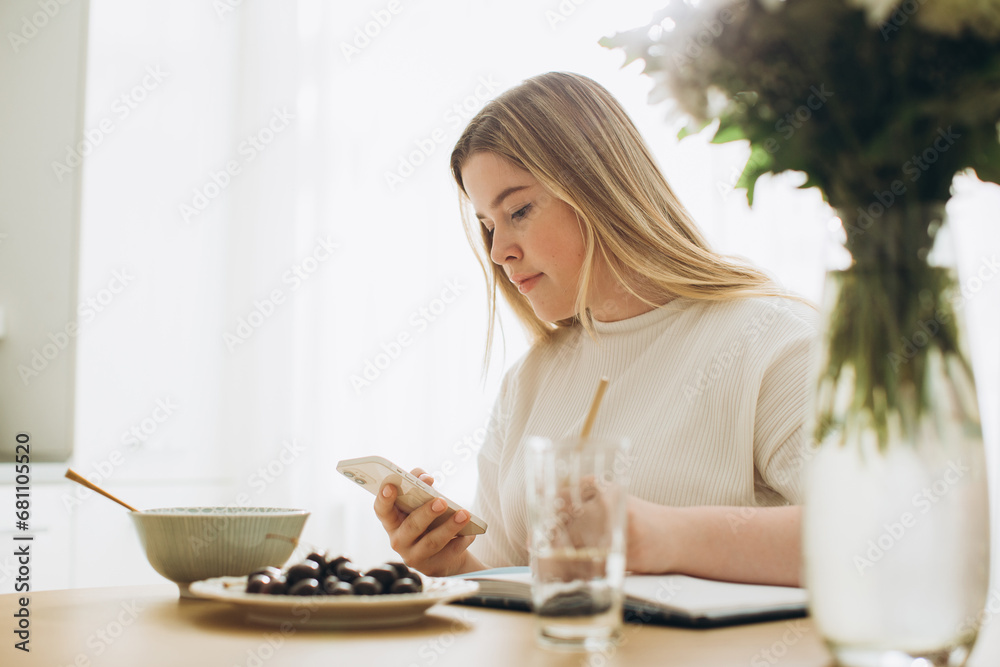 The blonde girl has breakfast while holding the phone in her hands. The blonde girl has breakfast while holding the phone in her hands.