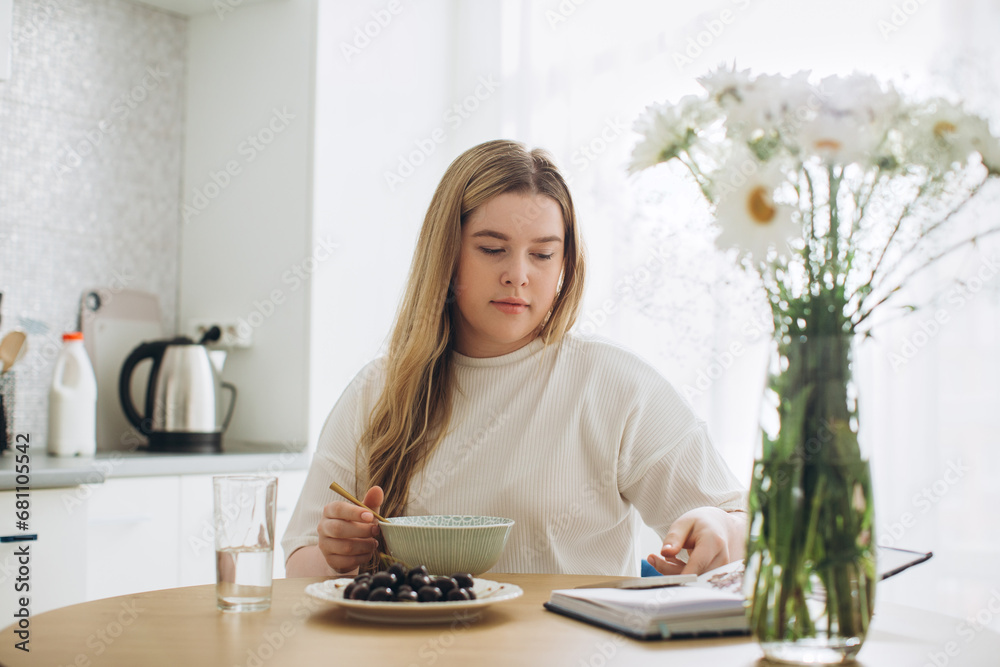 The blonde girl has breakfast while holding the phone in her hands. The blonde girl has breakfast while holding the phone in her hands.