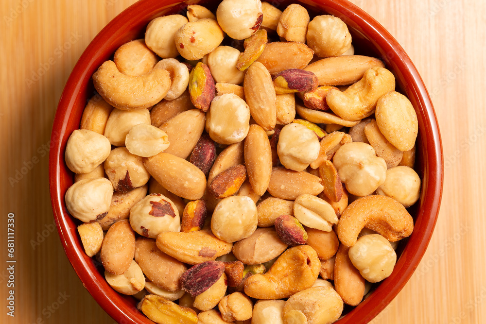 Roasted, peeled, salted peanuts, hazelnuts, cashews, almonds, pistachios. Mixed nuts in bowl on wooden background, top view.