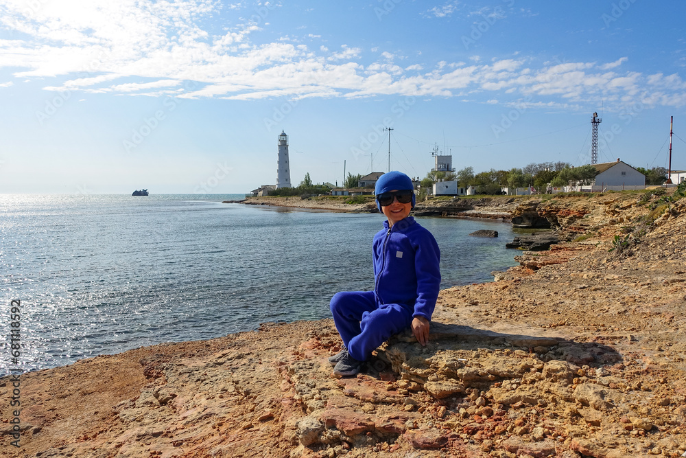 A boy on the background of a lighthouse on Cape Tarkhankut. The rocky coast of the Dzhangul Reserve in the Crimea. Turquoise sea water. Tarkhankutsky lighthouse on the Crimean peninsula.