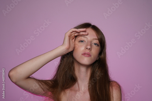 Portrait of longhaired woman in studio on pink background in pink neon light close up. Seminude woman looking straight ahead. Concept of beauty, cosmetology, care.