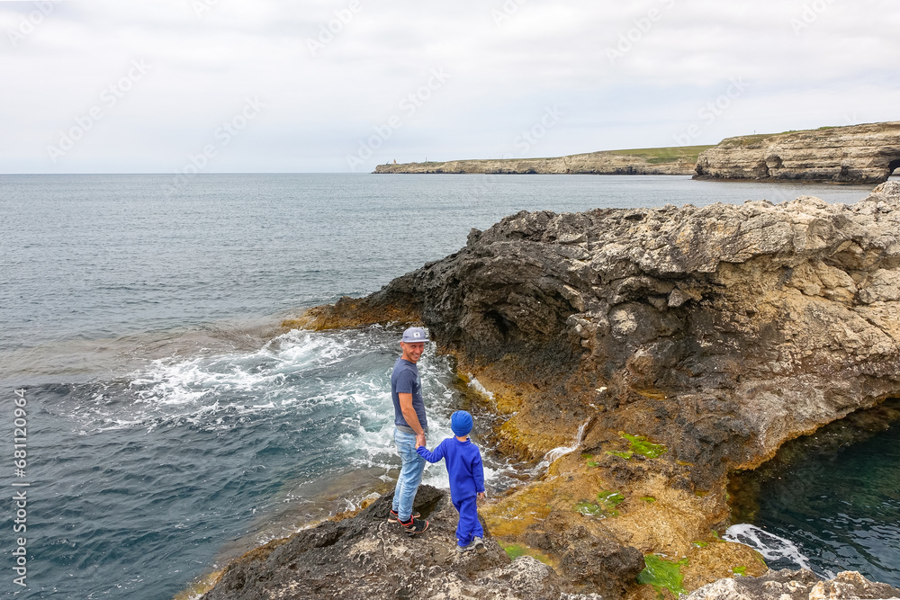 A man with a child on Cape Tarkhankut. The rocky coast of the Dzhangul Reserve in the Crimea. Turquoise sea water. Rocks and grottoes of Cape Tarkhankut on the Crimean peninsula.