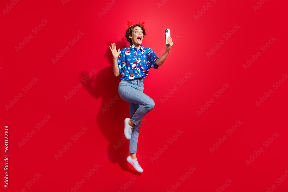 Full body photo jump girl of waving palm phone video greeting follower happy new year festive atmosphere isolated on red color background