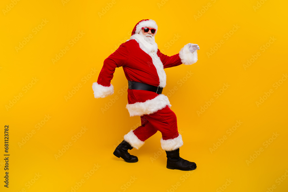 Full size profile portrait of eccentric aged santa claus sneaky walking christmas time isolated on yellow color background Full size profile portrait of eccentric aged santa claus sneaky walking christmas time isolated on yellow color background