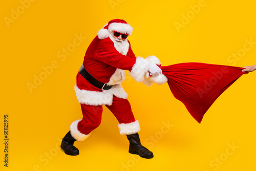 Full length portrait of santa compete person hand hold pull christmas gifts bag isolated on yellow color background