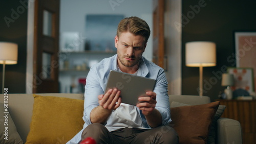 Focused hipster examining tab computer sitting couch. Man zooming pad screen photo