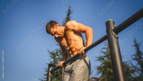 One man muscular male athlete training pull ups outdoor in sunny day