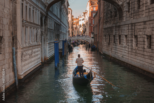 A scenic view of a gondola navigating a narrow canal in Venice, showcasing the city's iconic water transportation. The photo captures the timeless charm of the historic Italian city. © Aerial Film Studio