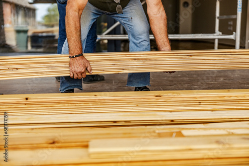 Cropped picture of a worker carrying wooden material on building site.