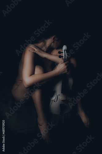 Nude girl with a beautiful body in the twilight with a white violin
