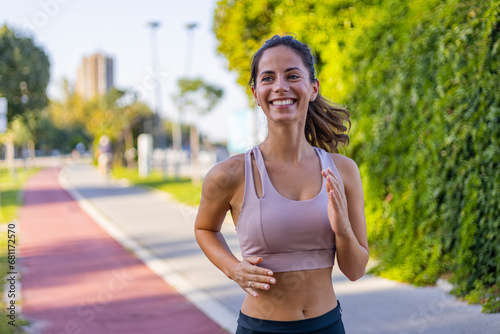 Happy slim woman wearing sportswear jogging in the city at sunrise. Young beautiful female in sports bra running outdoor. Workout exercise in the morning. Healthy and active lifestyle concept.