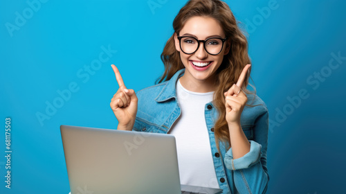 Cheerful young woman sitting in front of a laptop and pointing upwards with finger