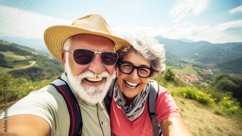 Happy senior couple making selfie, achievement of reaching the mountain summit, greenery and a panoramic view of the mountain range, story of active seniors embracing great outdoors