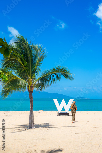 Seascape. A woman walks on a white sand beach near the sea with a palm tree and the letter W. Travel and tourism.