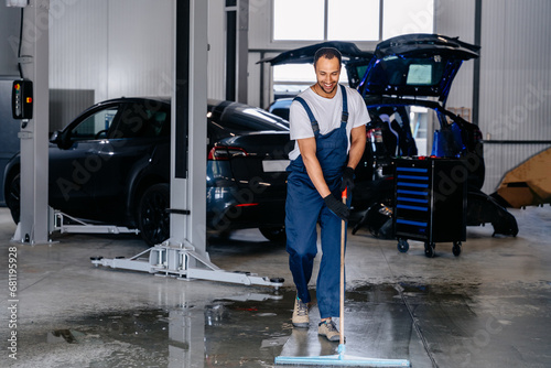 Arabian service staff man using a mop to remove water in the uniform cleaning the protective clothing of the new epoxy floor in an empty warehouse or car service center. photo