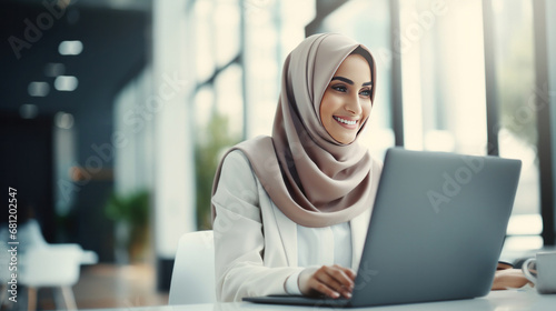 A happy muslim businesswoman in hijab at office workplace. Smiling Arabic woman working on laptop in a modern office. photo