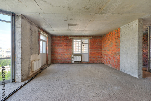 Empty living room without renovation, no repair in a new apartment building. Living room with concrete and red brick walls, concrete ceiling and floor, no plaster