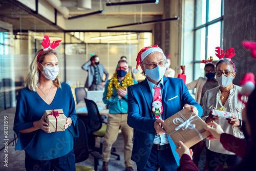 Business colleagues giving Christmas present to each other in office photo