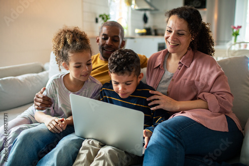 Happy family sitting on couch together using laptop at home photo
