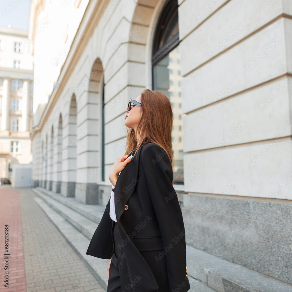 Elegant beautiful fashion brunette girl in fashionable business clothes with a black blazer walks near a vintage building in the city. Pretty urban chic woman Elegant beautiful fashion brunette girl in fashionable business clothes with a black blazer walks near a vintage building in the city. Pretty urban chic woman