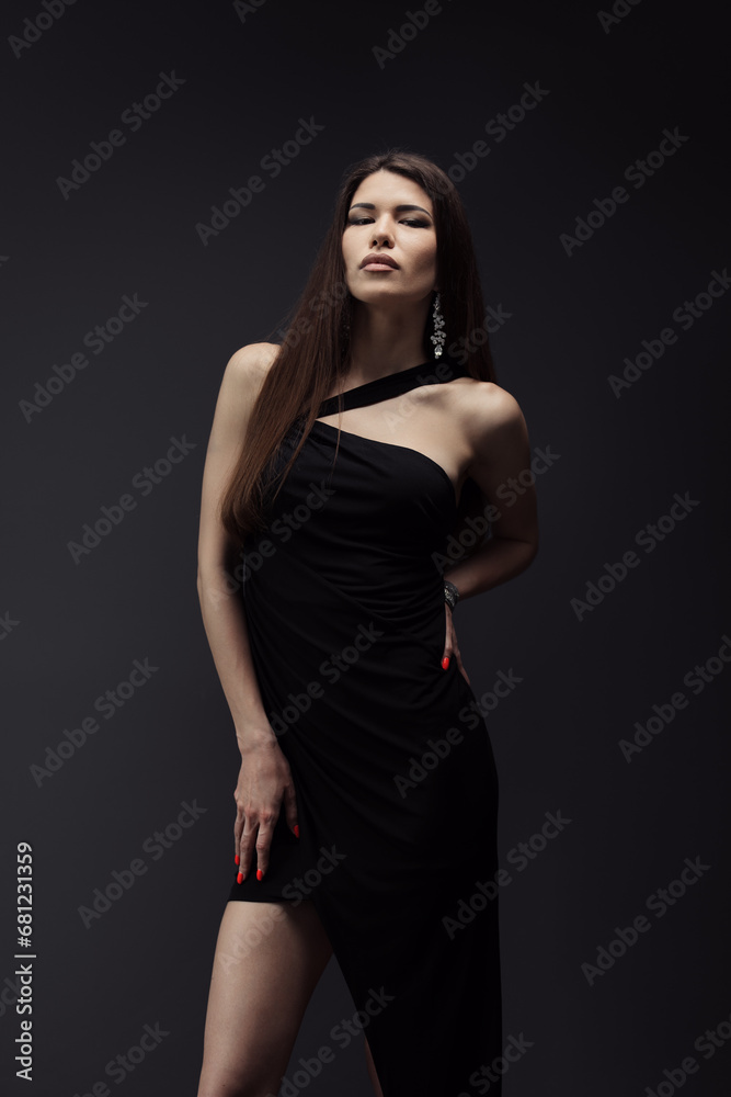 A stunning model poses in an asymmetrical black dress, her red nail polish complementing her striking appearance against a dark backdrop