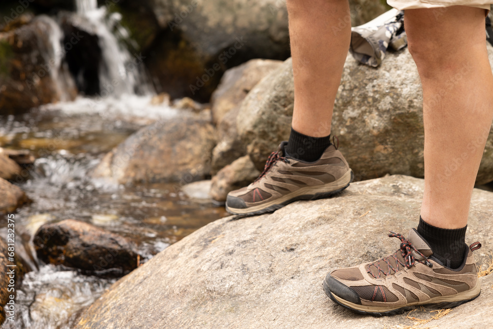 legs of man in hiking boots trekking over rocks with river and waterfall in background legs of man in hiking boots trekking over rocks with river and waterfall in background