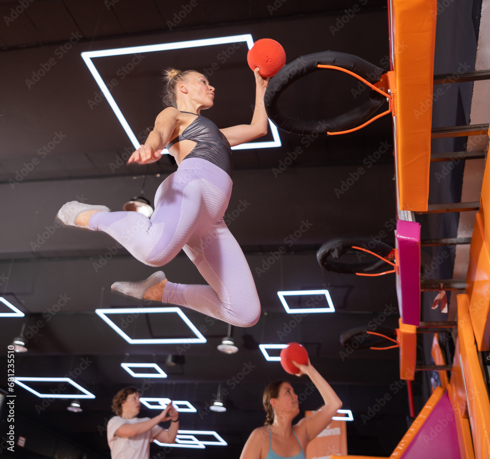 Dynamic middle-age woman throwing ball in basket while high jumping in ...