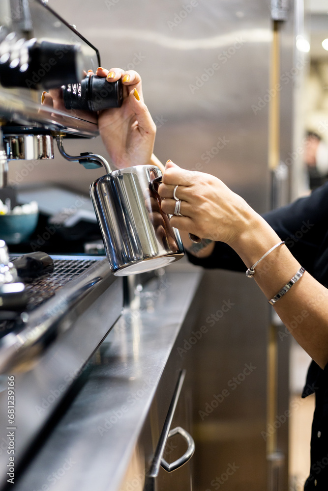 Vertical photo of an unrecognizable waitress heating milk with the frother of a coffee machine in the interior of a restaurant.Making milk steam with steam.Heating milk with a coffee machine.