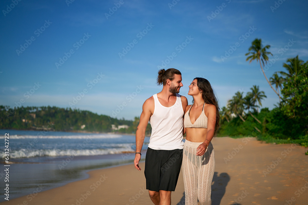 Romantic couple walks on beach at sunset, barefoot man, woman in casual summer clothes enjoy seaside stroll. Loving pair on vacation, leisure travel, coastline wander, tropical getaway, relaxed mood. Romantic couple walks on beach at sunset, barefoot man, woman in casual summer clothes enjoy seaside stroll. Loving pair on vacation, leisure travel, coastline wander, tropical getaway, relaxed mood.