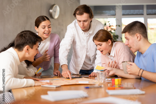 Group of interested grown-up students playing table game enthusiastically around large desk