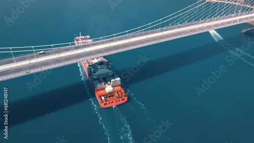 A large container ship sails under the YSS Cable Bridge. 300 meters long cargo vessel heading towards the Istanbul. Aerial Bosphorus Sea. 
