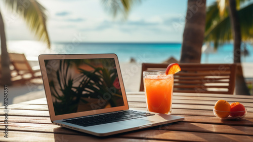 Laptop and cocktail on table, beach in the background